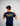 Person wearing a navy blue t-shirt with 'Creators of Champions Est. 1985' text on the back against a gray background