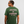 Man wearing a green t-shirt with 'Creators of Champions' text on the back against a light gray background
