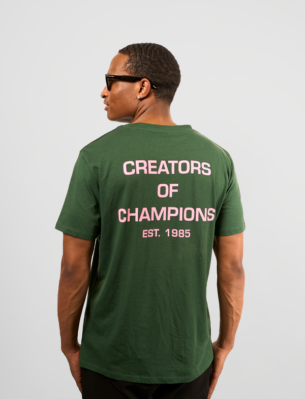 Man wearing a green t-shirt with 'Creators of Champions' text on the back against a light gray background