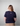 Person wearing a navy blue t-shirt with a logo on the back against a gray background