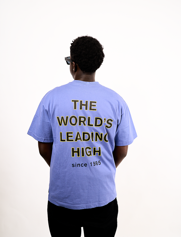 Person wearing a light blue t-shirt with "THE WORLDS LEADING HIGH"text on the back, standing against a white background
