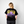 Person wearing a black Greenhouse Propaganda t-shirt with a yellow and purple design on the back, standing against a plain background.