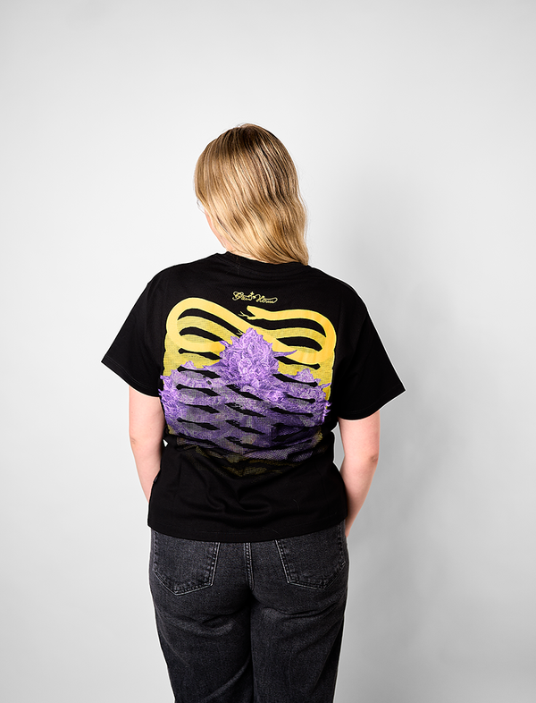Person wearing a black Greenhouse Propaganda t-shirt with a yellow and purple design on the back, standing against a plain background.