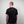 Man wearing a black t-shirt with a Greenhouse logo on the back against a plain background