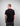 Man wearing a black t-shirt with a Greenhouse logo on the back against a plain background