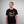 Person wearing a black t-shirt with yellow text and logo of Greenhouse Bangkokon a gray background