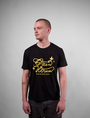 Person wearing a black t-shirt with yellow text and logo of Greenhouse Bangkokon a gray background