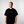 Man wearing a black t-shirt with a yellow logo on a plain background