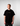 Man wearing a black t-shirt with a yellow logo on a plain background