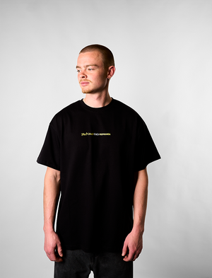 Man wearing a black t-shirt with a yellow logo on a plain background