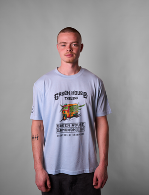 Person wearing a light blue Green House Light Blue TUKTUK t-shirt with a graphic design on a gray background