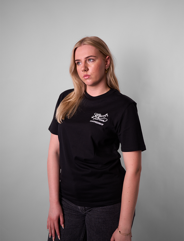 Person wearing a Green House World Cities T-Shirt Black with a logo on a gray background
