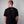 Person wearing a black t-shirt with a greehouse logo on the back against a gray background