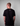 Person wearing a black t-shirt with a greehouse logo on the back against a gray background